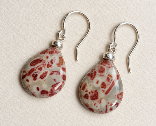 Handcrafted drop earrings with red and cream patterned stones on a warm ivory background.