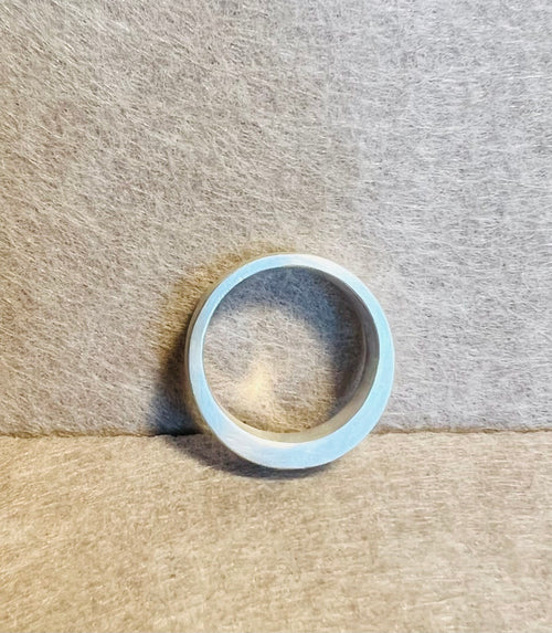 Silver-colored band ring standing upright, showing its circular profile and inner surface against textured neutral fabric.